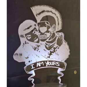 lámpara de acrílico mostrando una pareja abrazada; ella es una mujer con el pelo largo y él un esqueleto con un mohawk, con la frase "I AM YOURS" (Soy tuyo/a) en la base.
