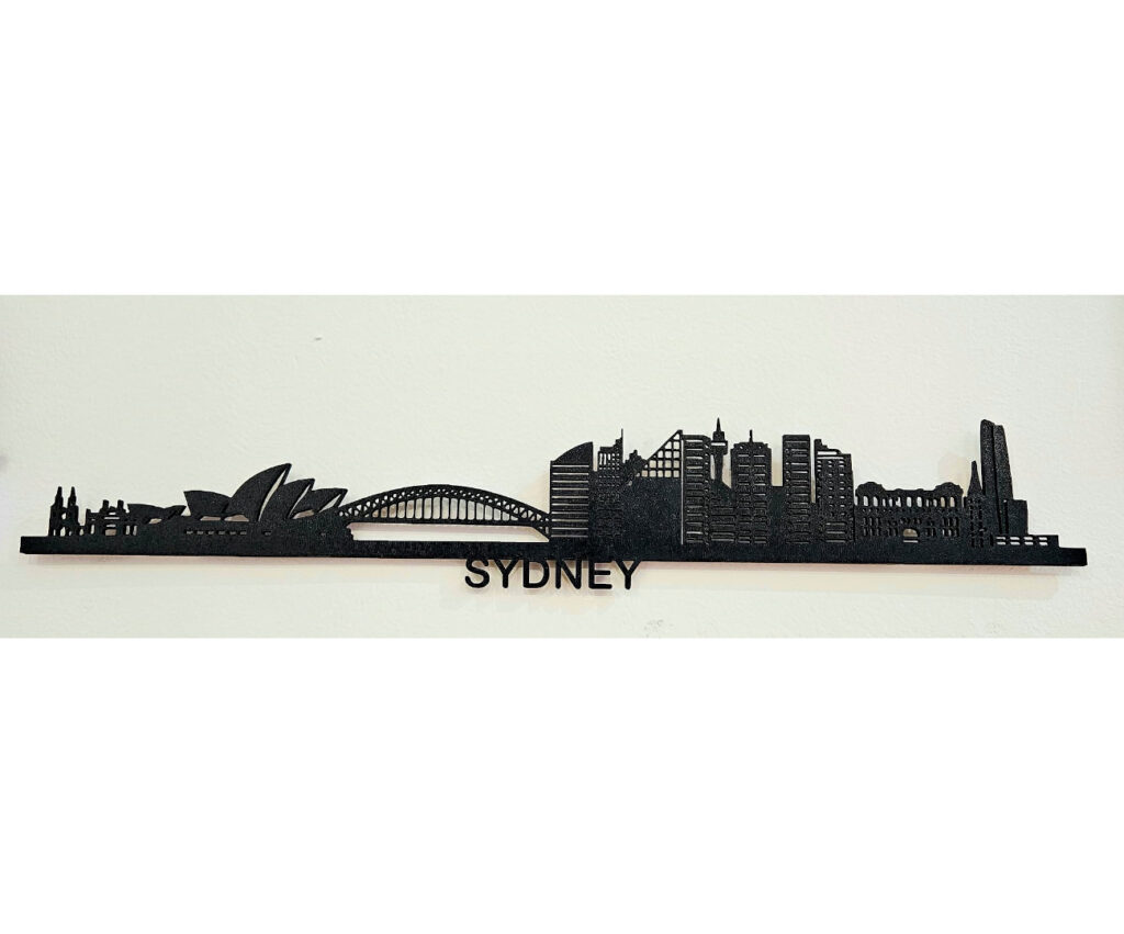 La imagen muestra un contorno de la silueta de la ciudad de Sídney, con algunos iconos arquitectónicos destacados como la Ópera de Sídney y el Puente del Puerto. La palabra "SYDNEY" aparece en la parte inferior del diseño.